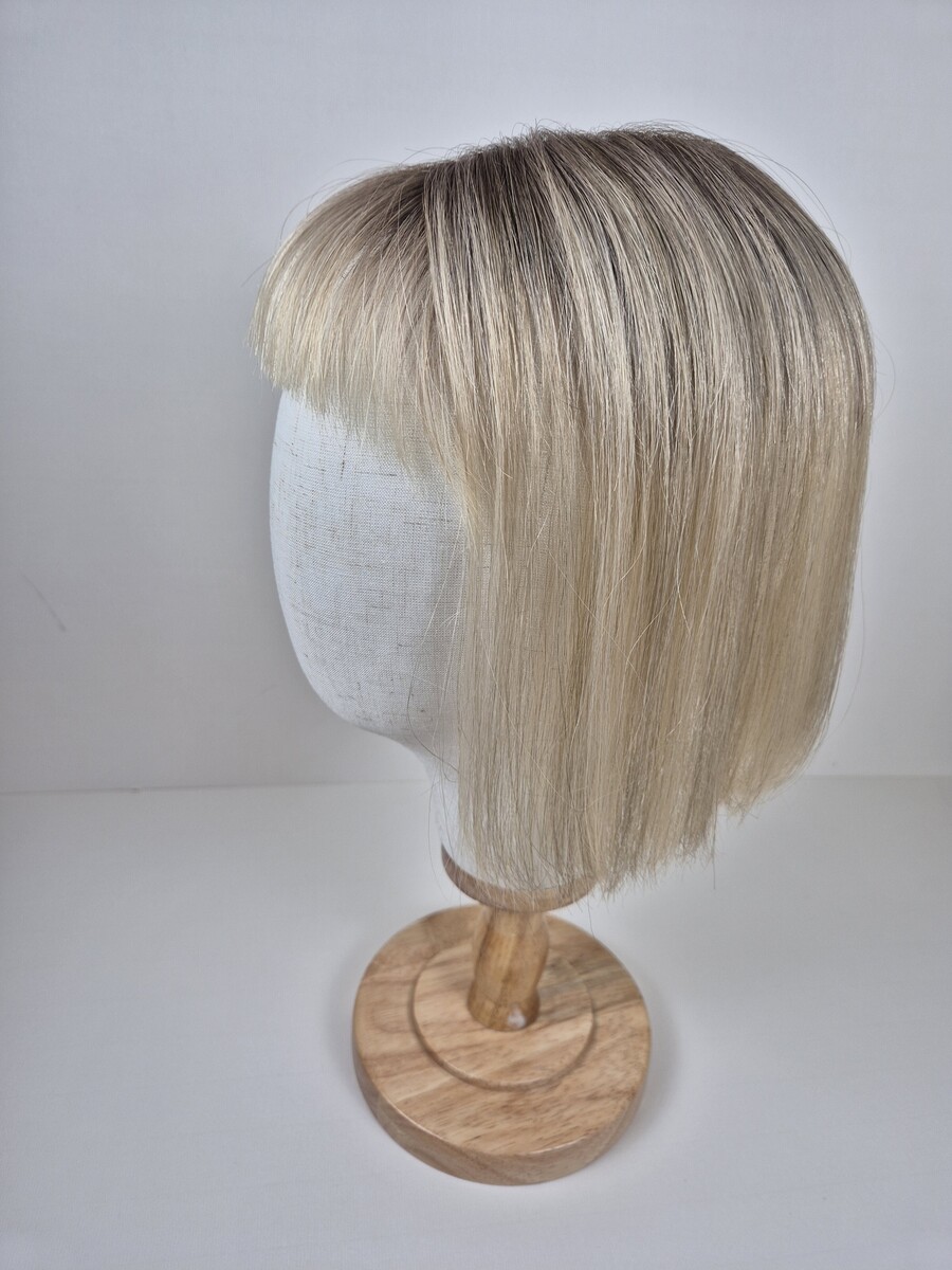 Cora Tiny Topper 11 inch length a creamy blonde with a soft ash root. styled straight with a fringe displayed on a mannequin